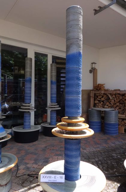 Designerbrunnen vom Künstler mit gerillter Säule und kaskadenförmiges Abtropfen über Teller, dezente Akustik blau-sand