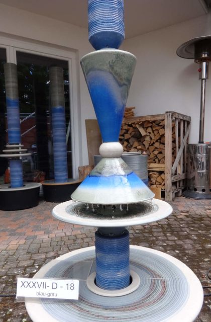 Designerbrunnen vom Künstler mit gerillter Säule und Lichtreflexen über zwei farbige Kegel, dezente Akustik blau-grau