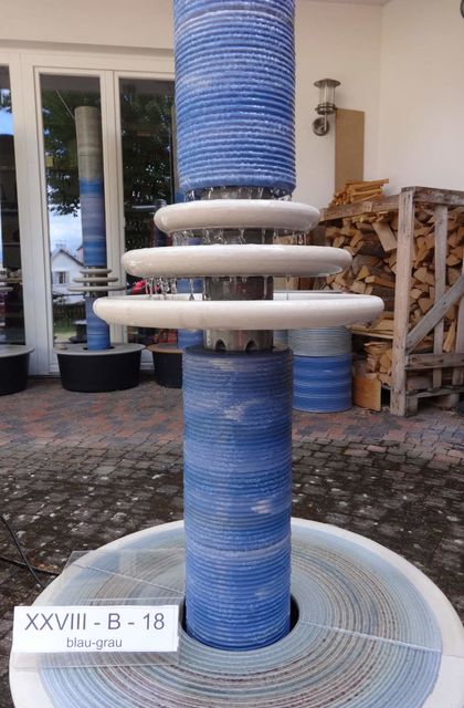 Designerbrunnen vom Künstler mit gerillter Säule und kaskadenförmiges Abtropfen über Teller, dezente Akustik blau-grau