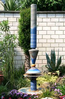 Moderner Gartenbrunnen aus winterfester Keramik mit gerillter Säule und Lichtreflexen über zwei farbige Kegel, dezente Akustik