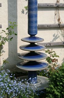Moderner Gartenbrunnen groß aus winterfester Keramik mit gerillter Säule und Lichtreflexen über vier farbige Kegel, dezente Akustik
